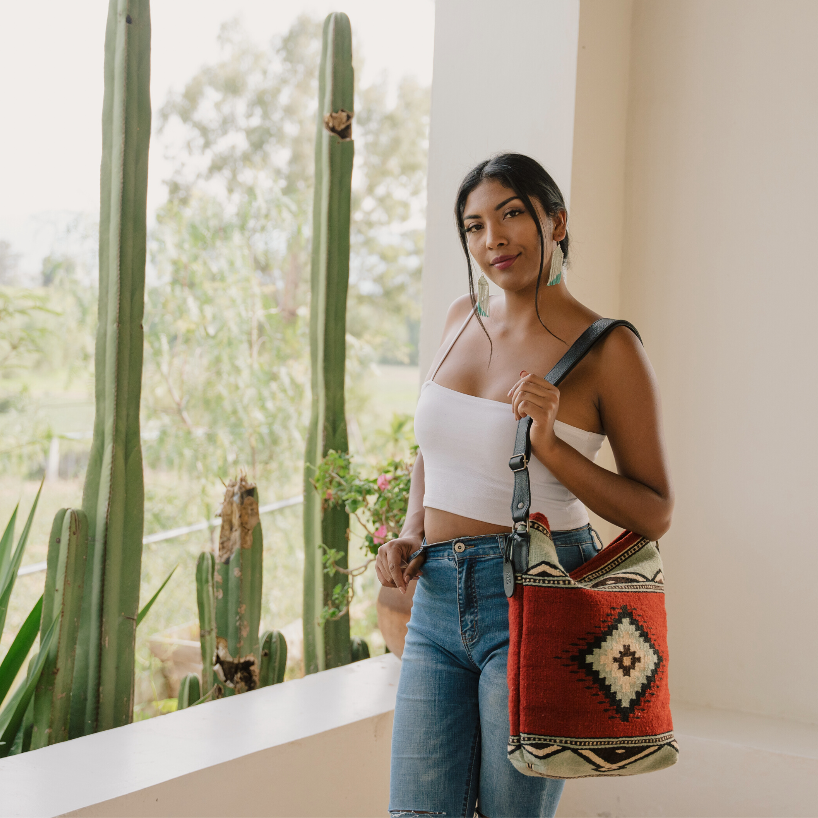 Fashionable woman with an AMASOUK handwoven wool convertible shoulder/crossbody bag in Adobe + Azul pattern, highlighted by a Zapotec design in adobe red and mint green. Ideal for day-to-night versatility.