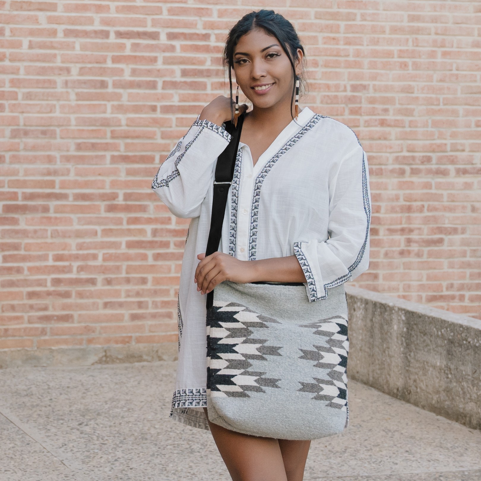 Woman carrying an AMASOUK handwoven wool convertible shoulder/crossbody bag with Leona name, featuring a Zapotec pattern in natural shades of charcoal, ivory, and stone. Perfect for errands, work, or casual outings.