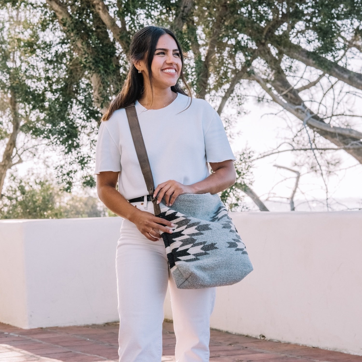 Woman with an AMASOUK handwoven wool convertible shoulder/crossbody bag in Leona pattern, showcasing a Zapotec design in neutral hues of pewter, alabaster, and deep ash. Perfect for everyday activities and evening events.