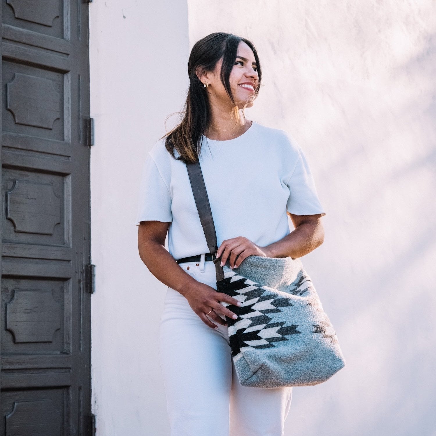 Effortlessly chic woman carrying an AMASOUK handwoven wool convertible shoulder/crossbody bag with Leona pattern and a Zapotec design in soft dove gray, cream, and jet black. A versatile accessory for any occasion.