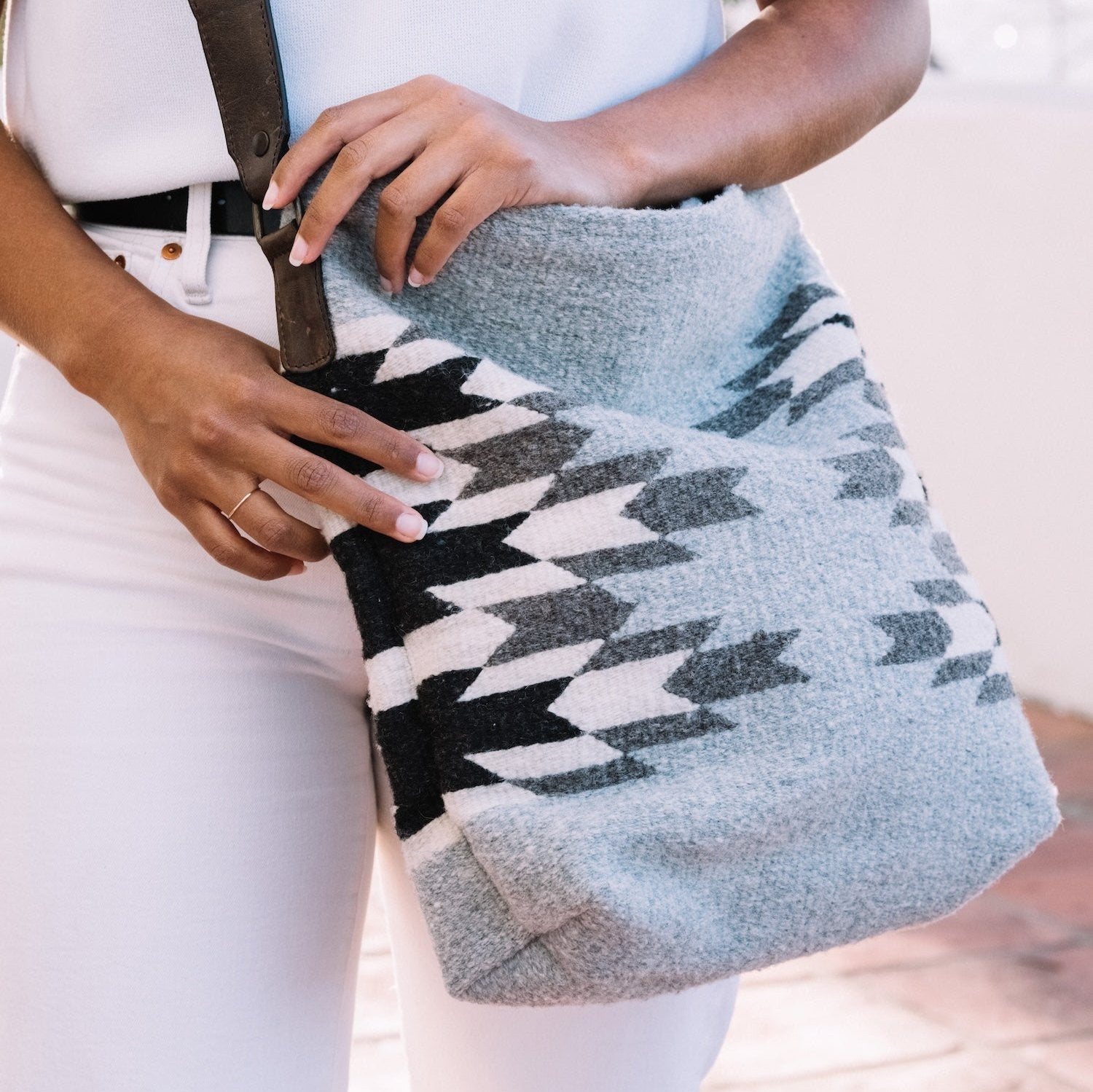 Effortlessly chic woman carrying an AMASOUK handwoven wool convertible shoulder/crossbody bag with Leona pattern and a Zapotec design in soft dove gray, cream, and jet black. A versatile accessory for any occasion.