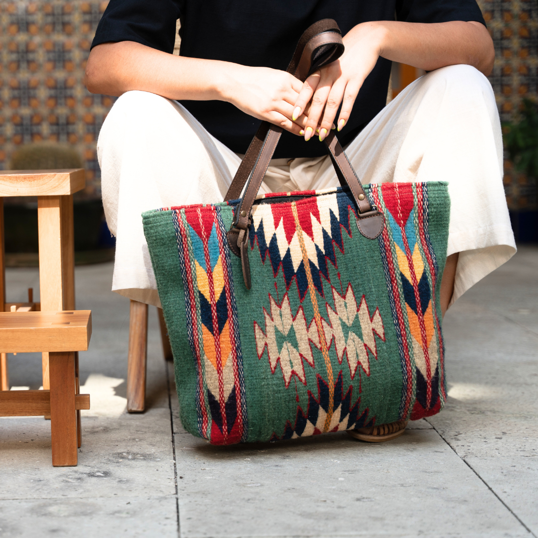 Woman with Handwoven wool tote bag in green and bold colors with Zapotec patterns, leather shoulder straps, and relaxed shape, roomy and ideal for everyday use. 