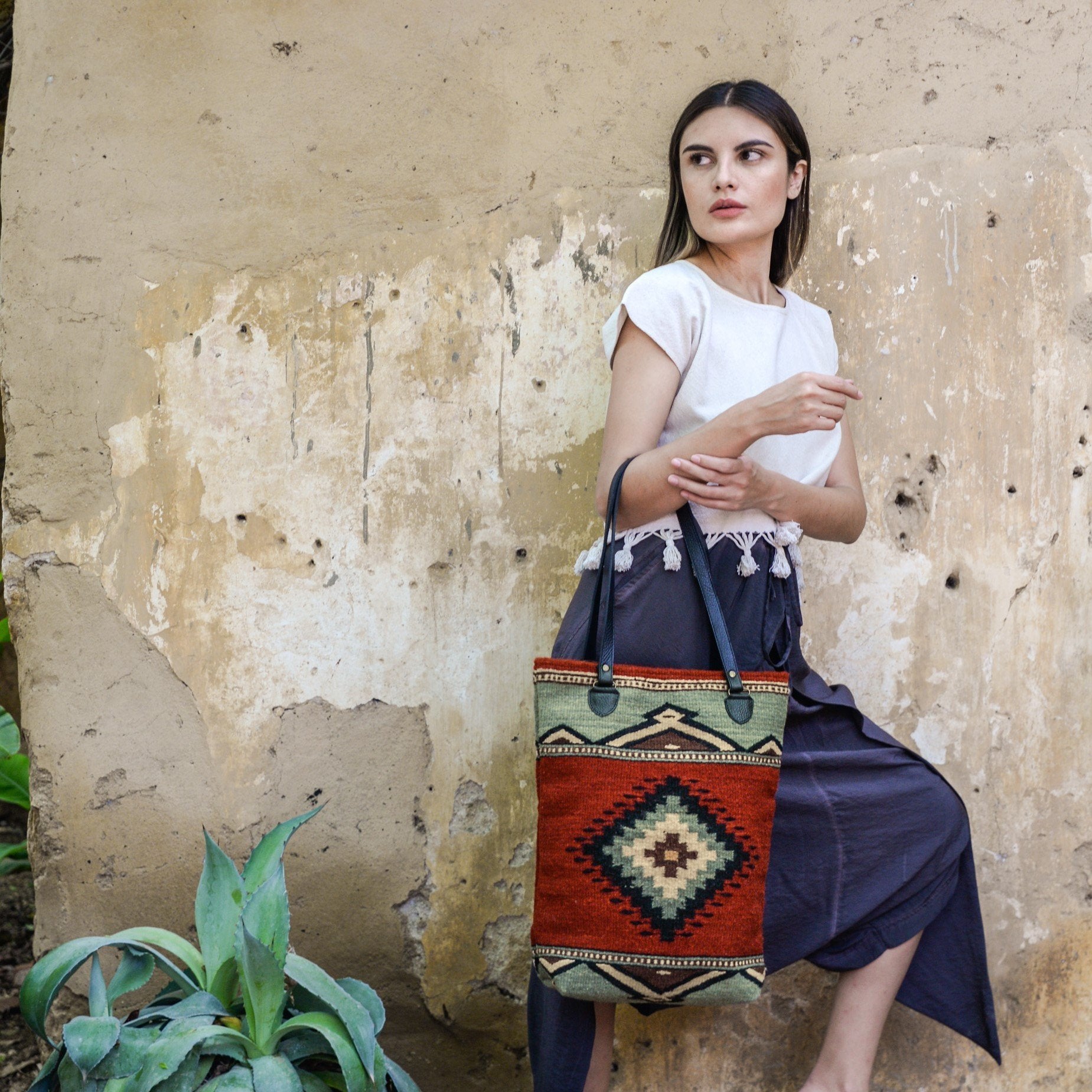 Effortlessly chic woman carrying an AMASOUK handwoven wool tote with Adobe + Azul pattern and a Zapotec design in adobe red and mint green. A versatile accessory for any occasion.