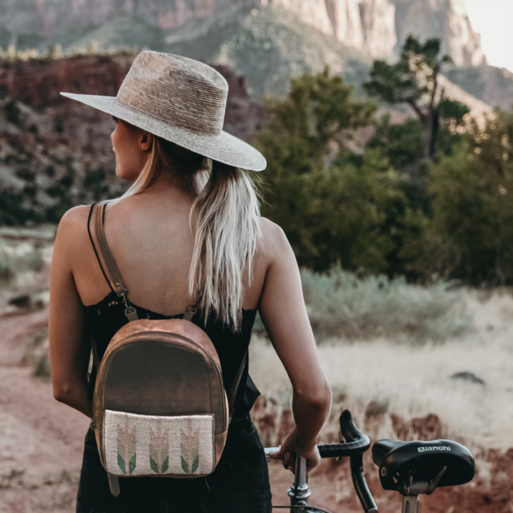 Fashionable woman carrying the AMASOUK Arbol Mini Backpack on a bike ride, made from brown leather and light green and cream wool. Perfect for day trips and casual outings.